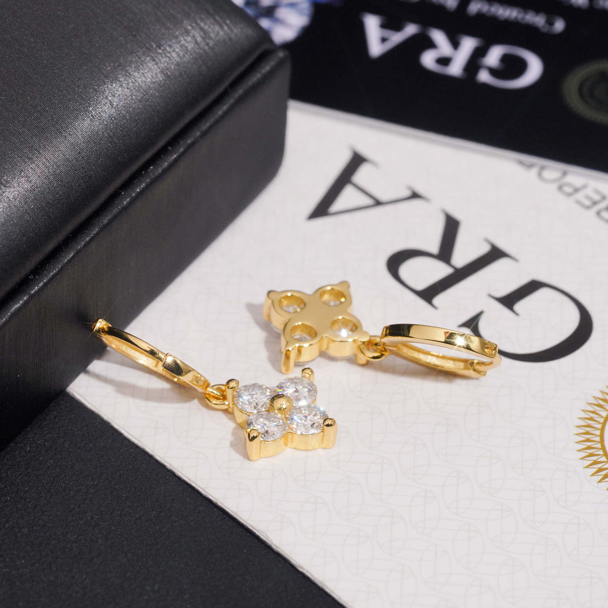 Yellow gold iced out four-leaf clover dangle huggie hoop moissanite earrings on GRA certificate card
