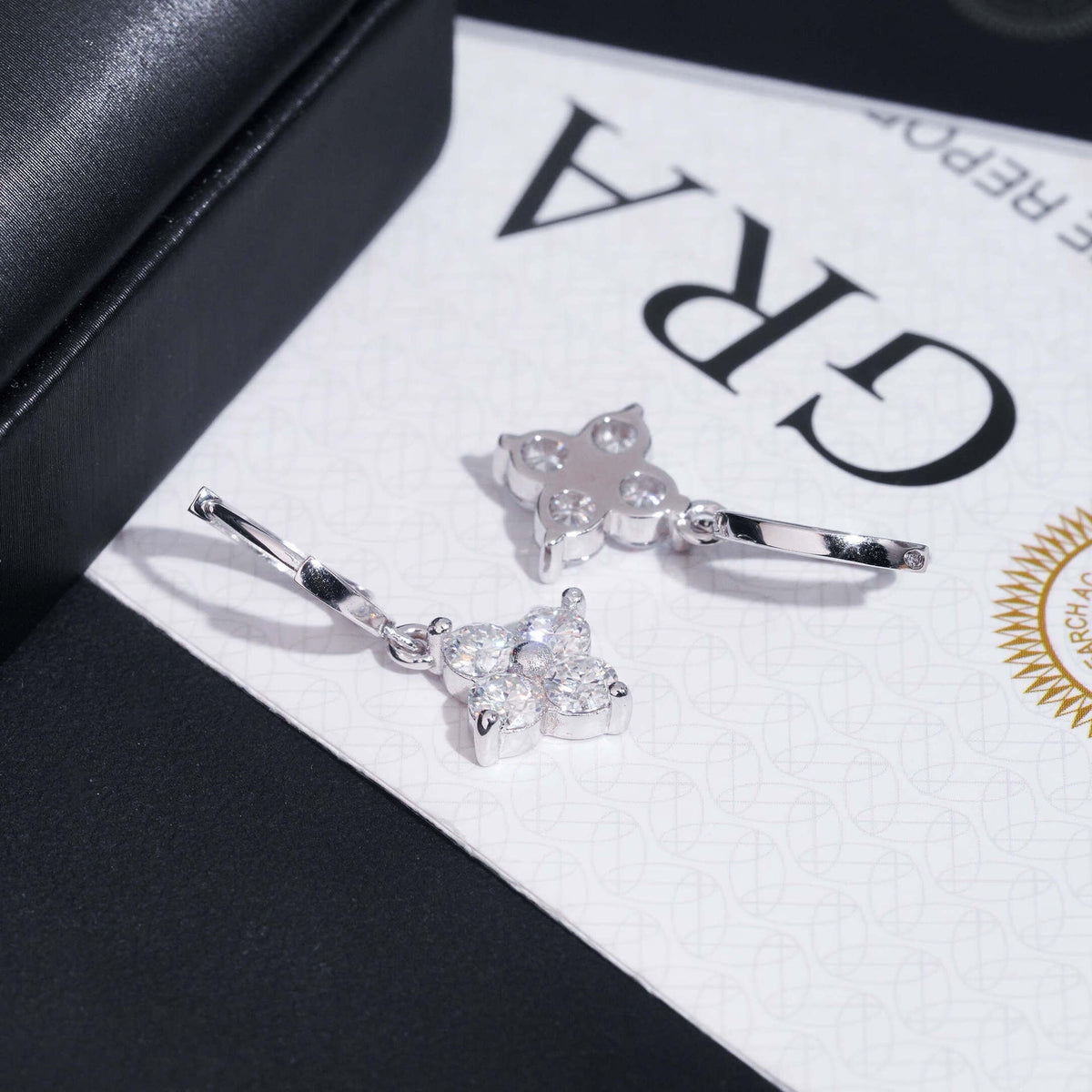 Silver iced out four-leaf clover dangle huggie hoop moissanite earrings displayed on GRA report card