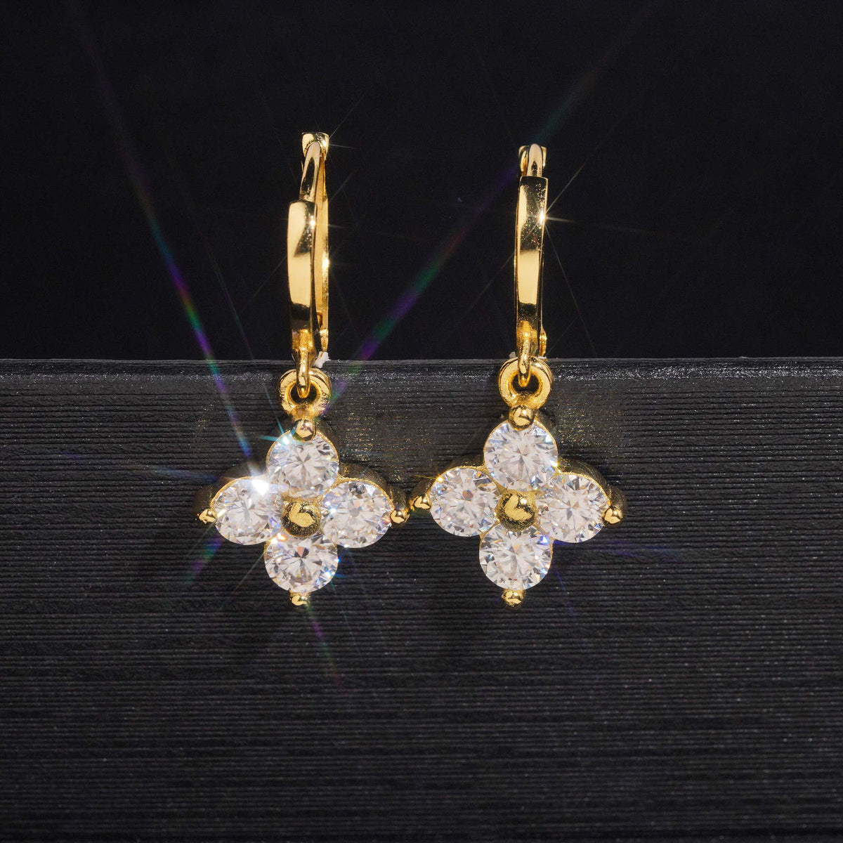 Pair of yellow gold iced out four-leaf clover dangle huggie hoop moissanite earrings showing hinged clasp