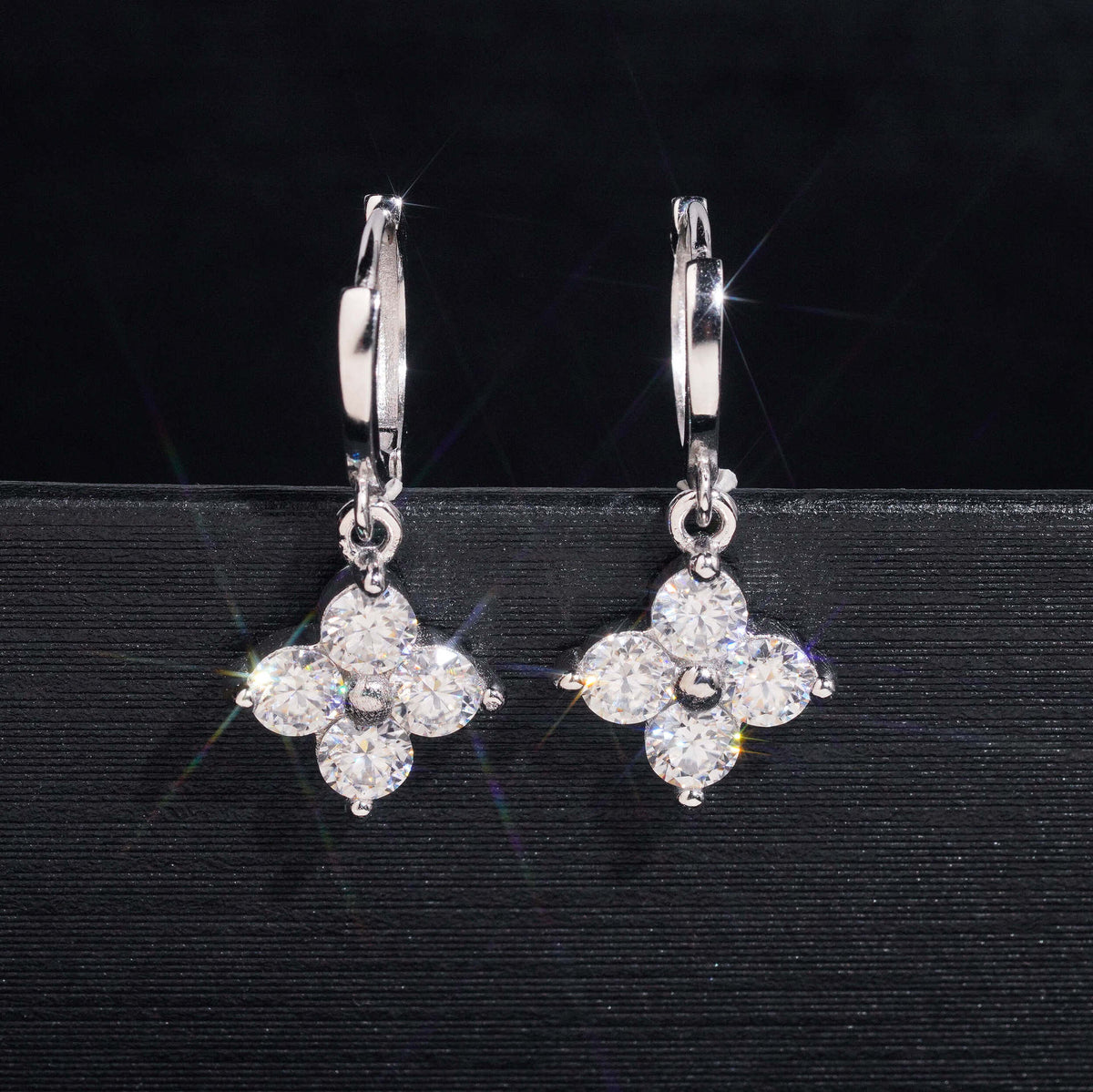 Pair of silver iced out four-leaf clover dangle huggie hoop moissanite earrings on dark background