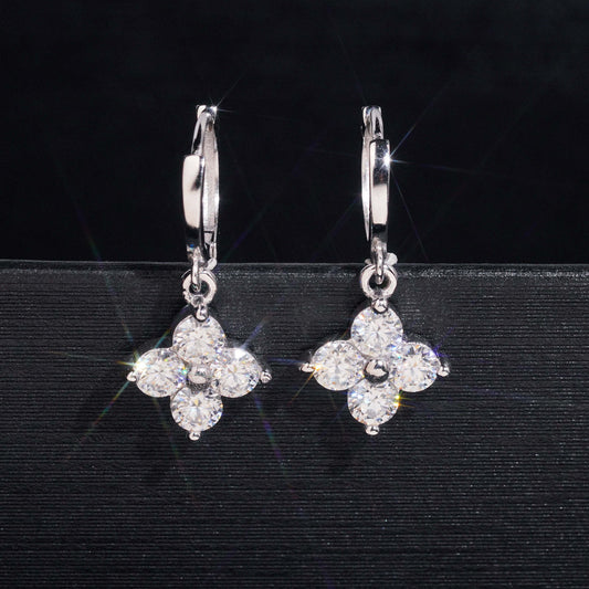Pair of silver iced out four-leaf clover dangle huggie hoop moissanite earrings on dark background