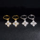 Iced out four-leaf clover dangle huggie hoop moissanite earrings in gold and silver on dark surface