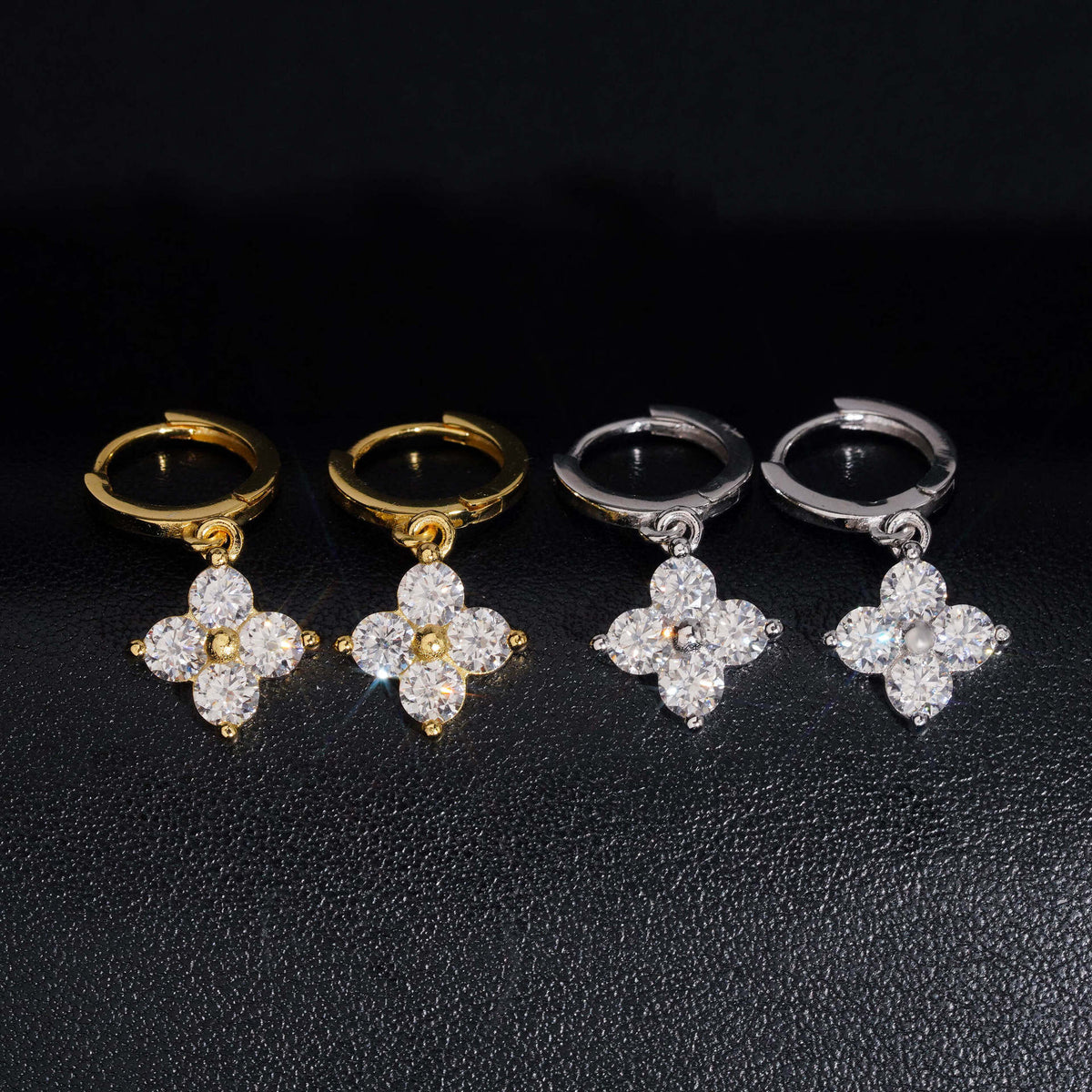 Iced out four-leaf clover dangle huggie hoop moissanite earrings in gold and silver on dark surface