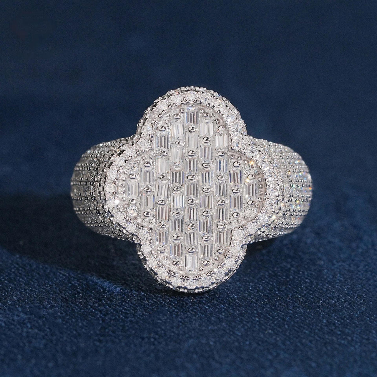 Iced out four-leaf clover moissanite baguette ring in sterling silver resting on dark blue surface