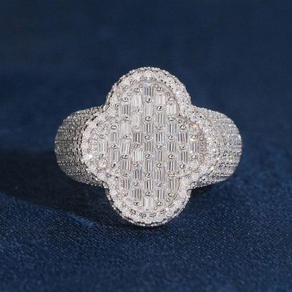 Iced out four-leaf clover moissanite baguette ring in sterling silver resting on dark blue surface
