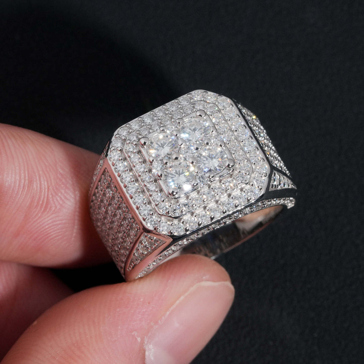 Angled view showing wide pave band and square cluster halo of moissanite ring on dark surface