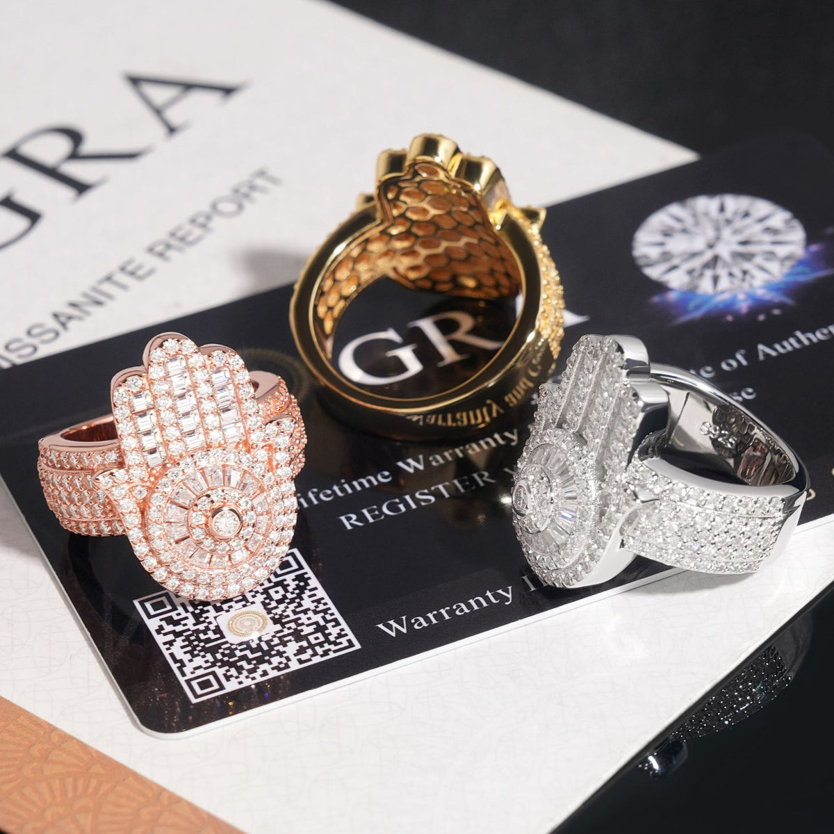 Iced out hamsa hand moissanite baguette statement rings displayed on GRA certificate card