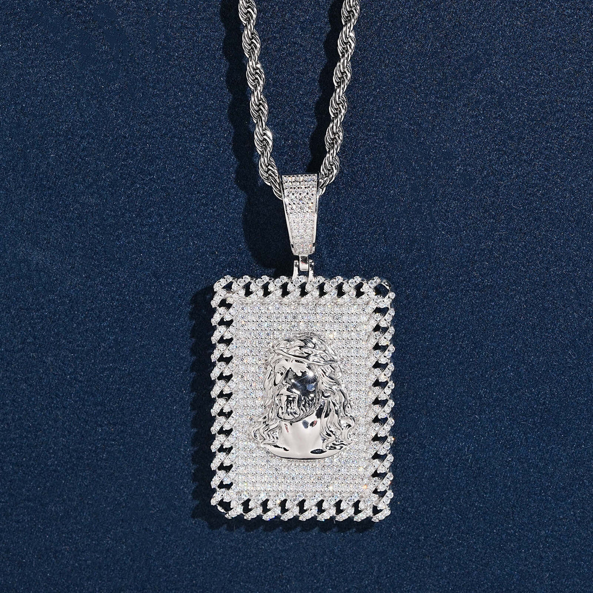 Iced out jesus piece moissanite dog tag pendant in sterling silver on rope chain resting on dark blue background