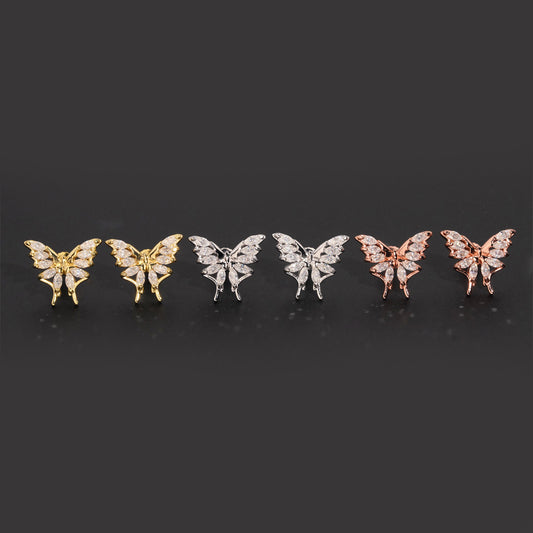 Iced out marquise butterfly moissanite stud earrings in yellow gold, silver, and rose gold on dark surface