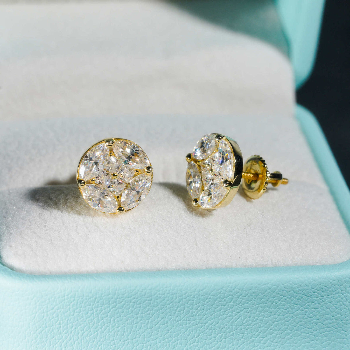 Pair of yellow gold iced out marquise cluster round moissanite stud earrings inside blue jewelry box
