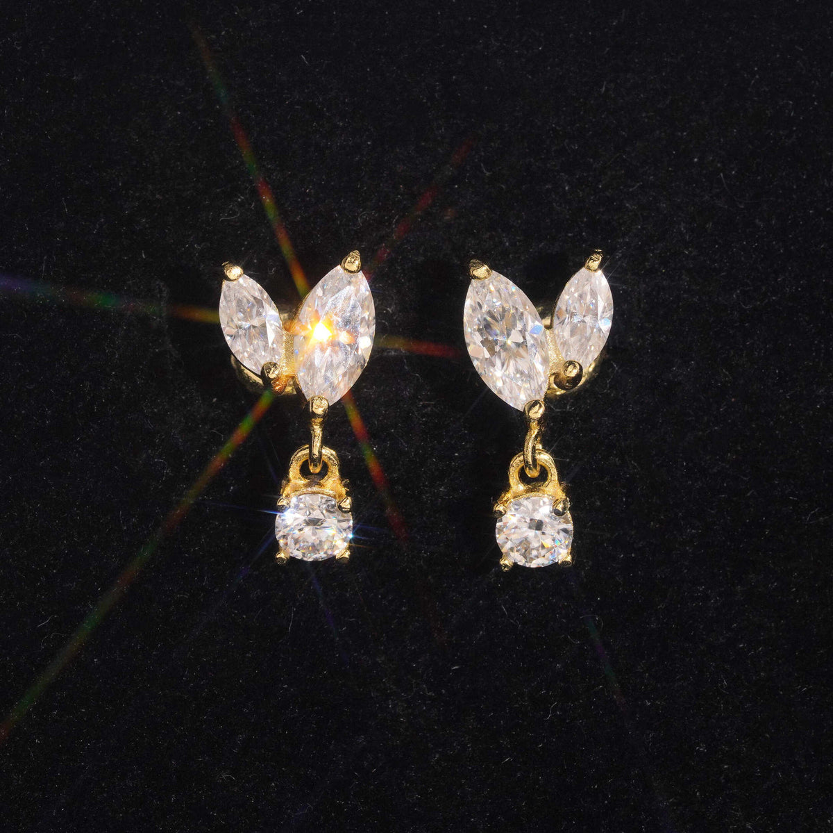 Yellow gold iced out marquise leaf dangle solitaire moissanite stud earrings sparkling on dark background