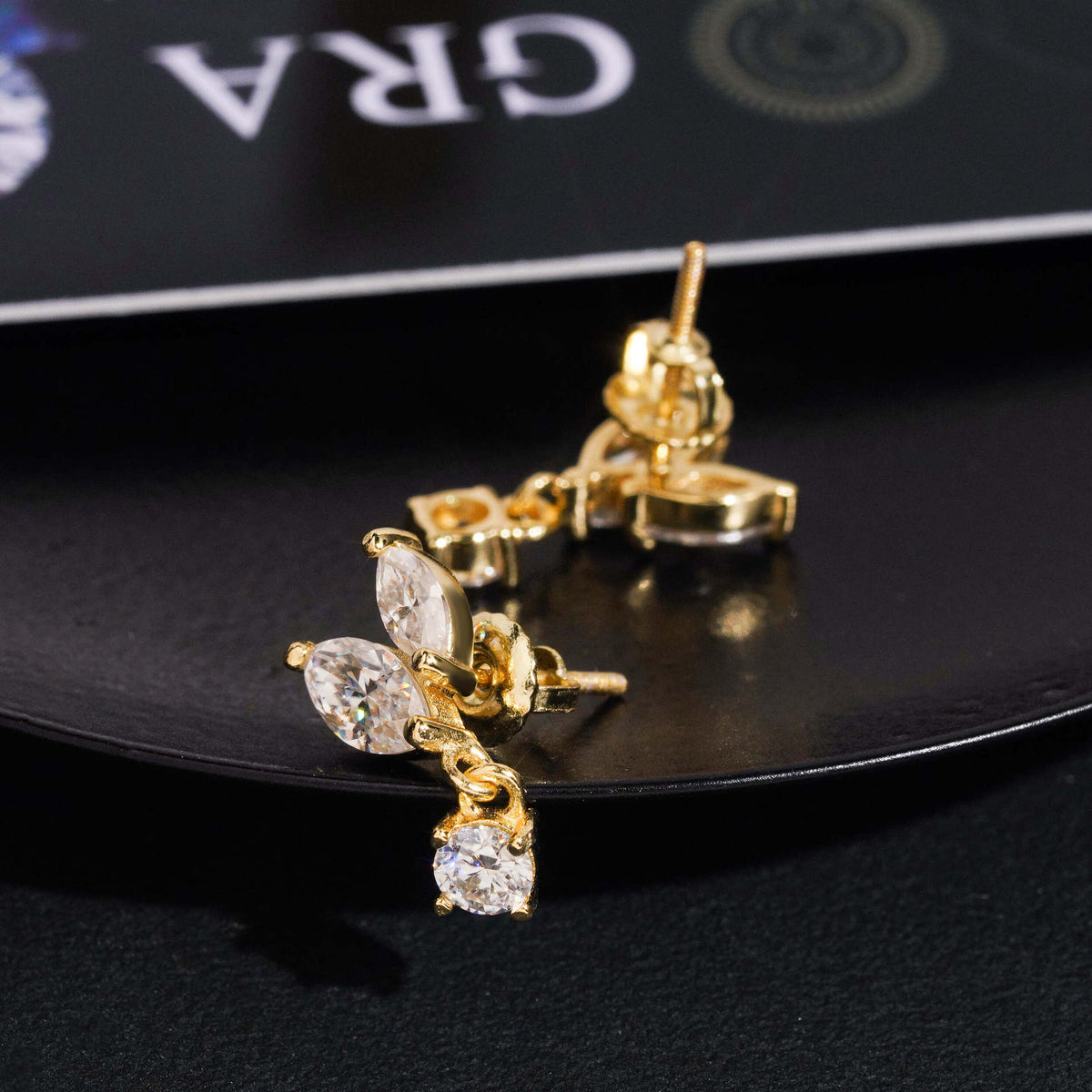 Gold iced out marquise leaf dangle solitaire moissanite stud earrings showing screw backs on GRA certificate card