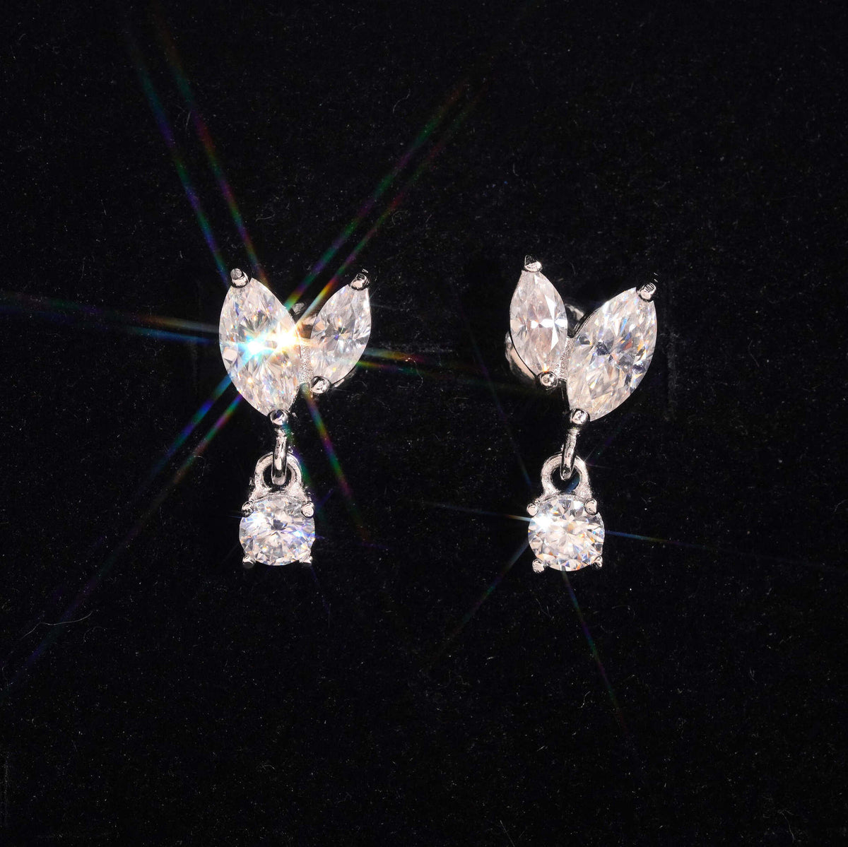 Silver iced out marquise leaf dangle solitaire moissanite stud earrings sparkling on dark background   