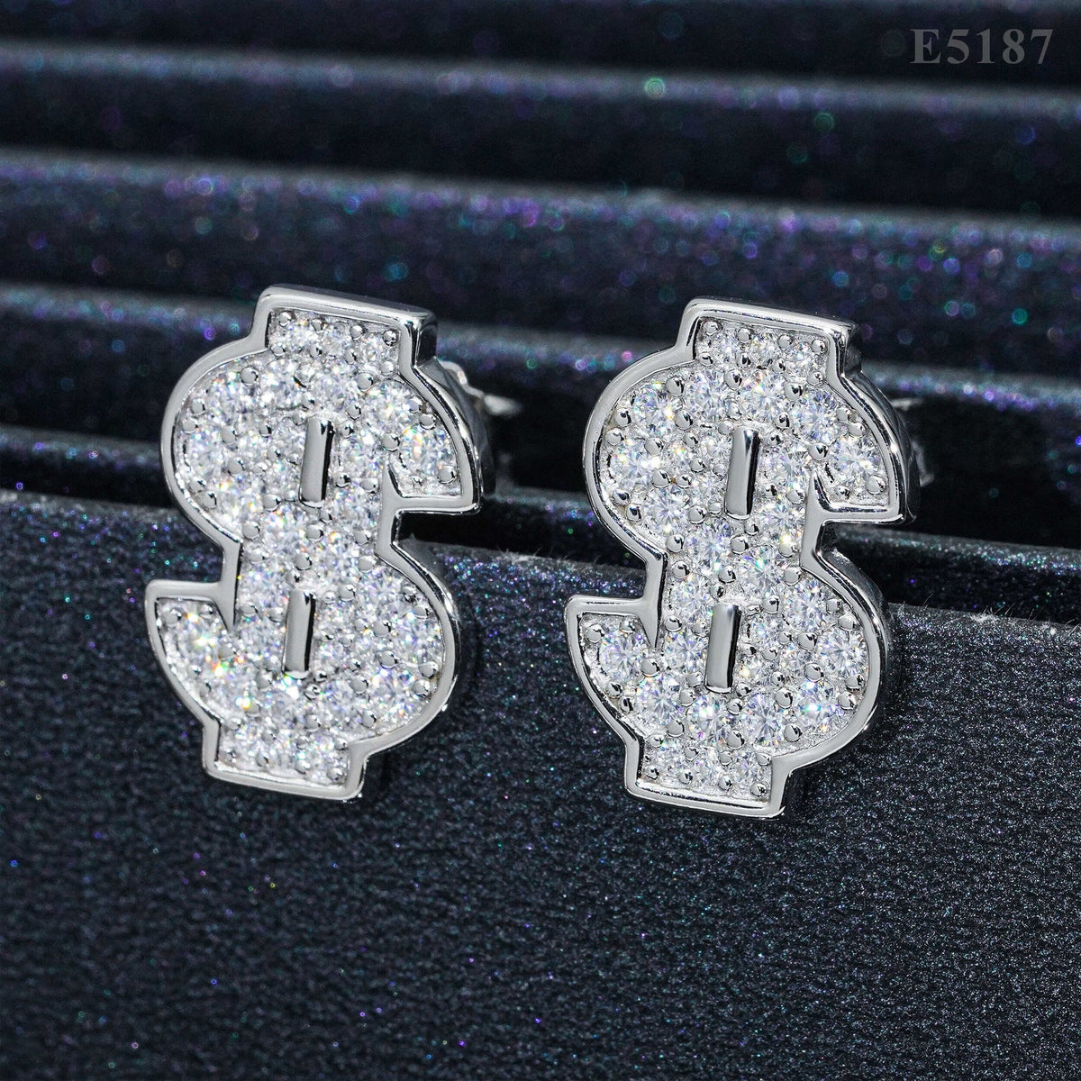 Silver iced out money sign dollar sign moissanite stud earrings aligned on black jewelry display stand