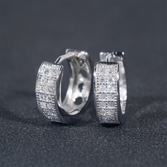 Iced out multi-row pave moissanite huggie hoop earrings in sterling silver resting on dark background