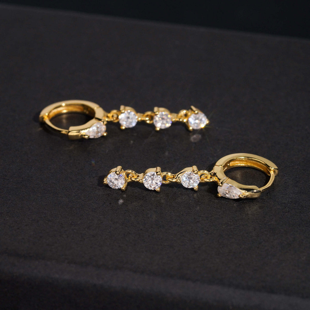 Yellow gold iced out pear cut and 3-stone drop dangle huggie hoop moissanite earrings on dark surface