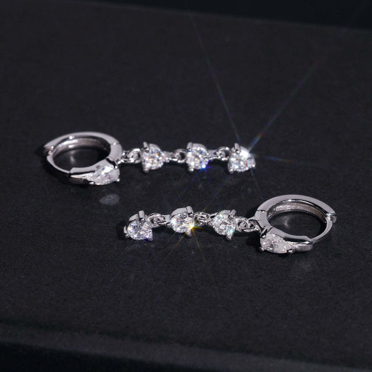 Silver iced out pear cut and 3-stone drop dangle huggie hoop moissanite earrings on dark background