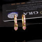 Yellow gold iced out pink heart dangle huggie hoop moissanite earrings in front of GRA certificate card