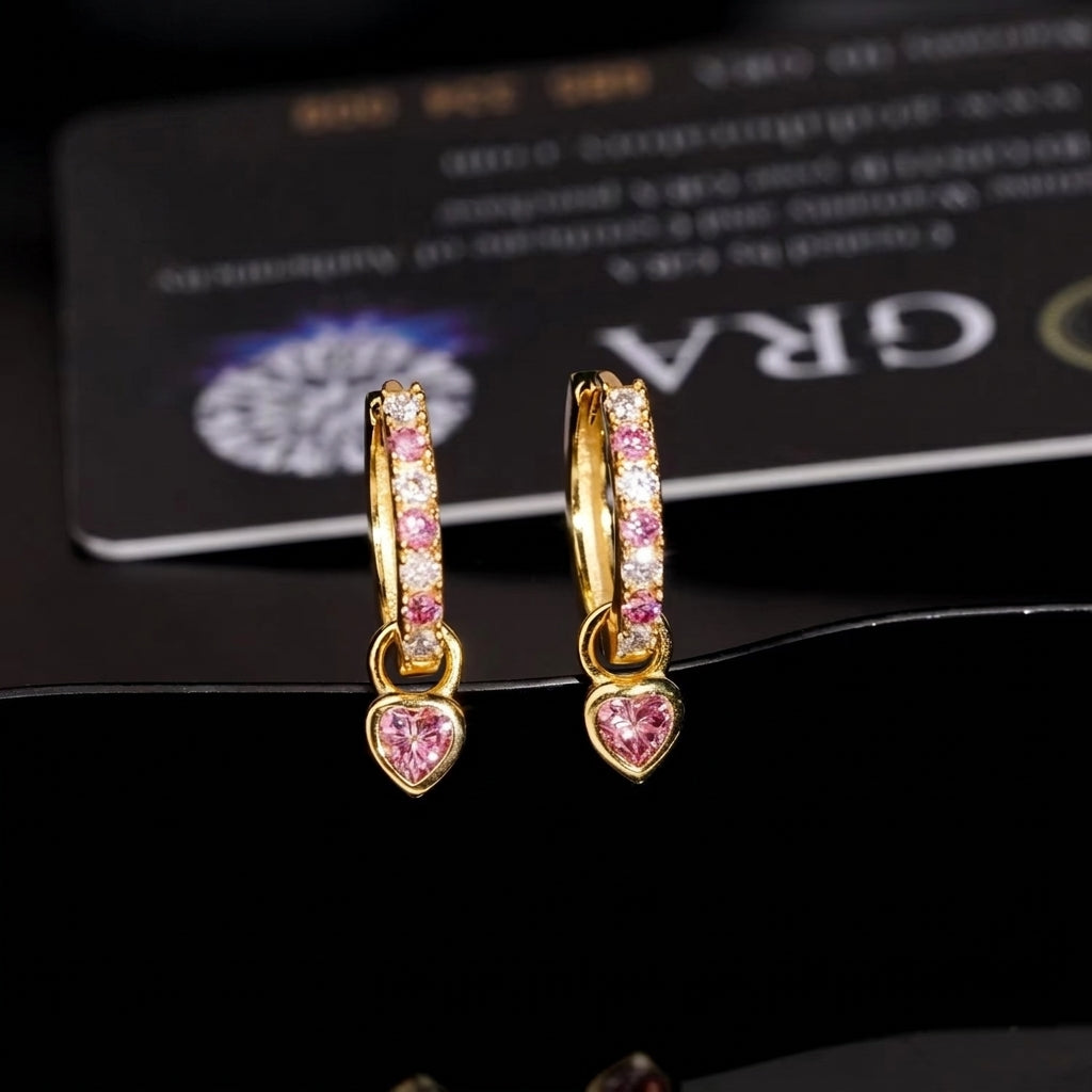 Yellow gold iced out pink heart dangle huggie hoop moissanite earrings in front of GRA certificate card