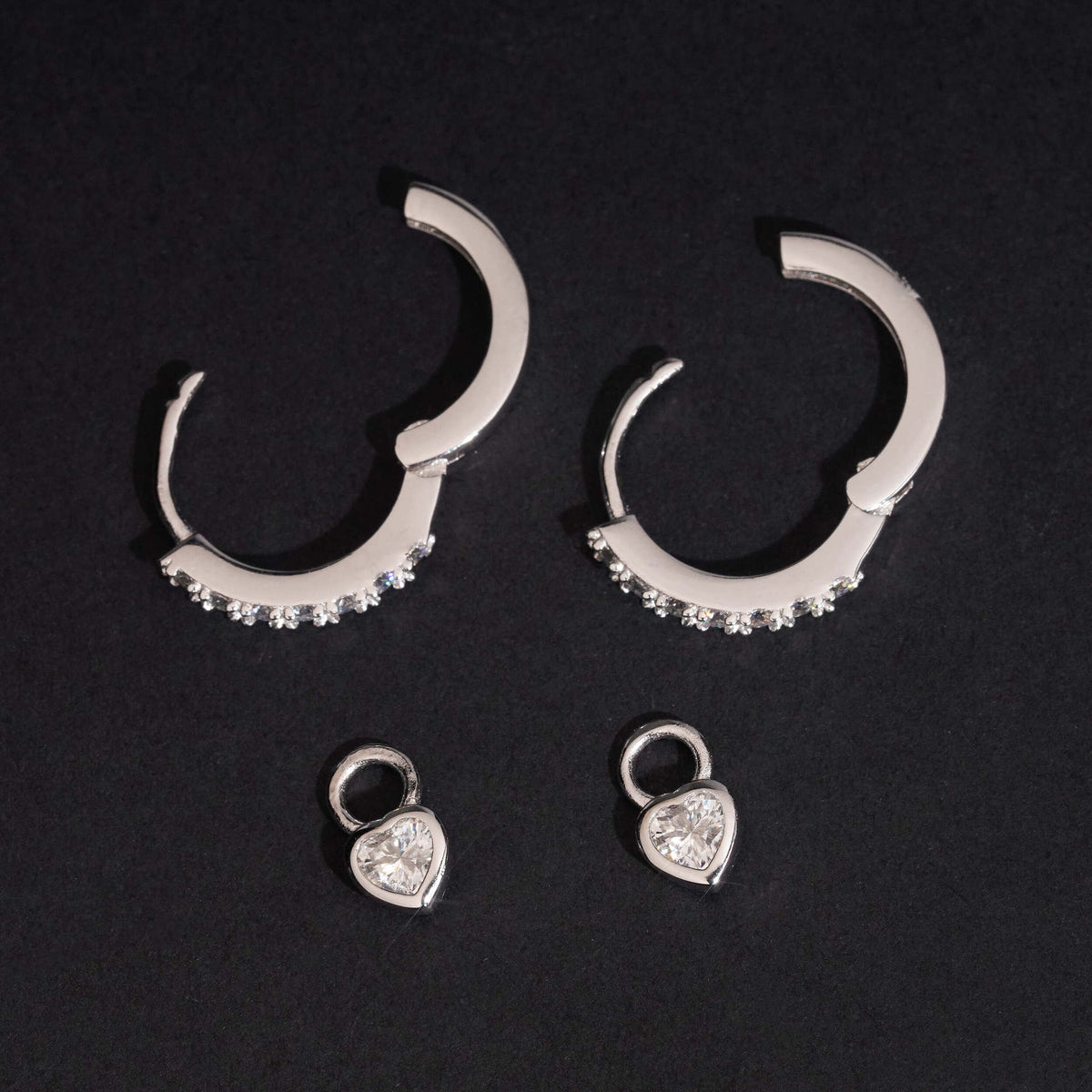 Pair of silver iced out pink heart dangle huggie hoop moissanite earrings on dark display stand