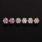 Iced out pink and white flower 7-stone cluster moissanite stud earrings in pink, silver, and gold on dark surface