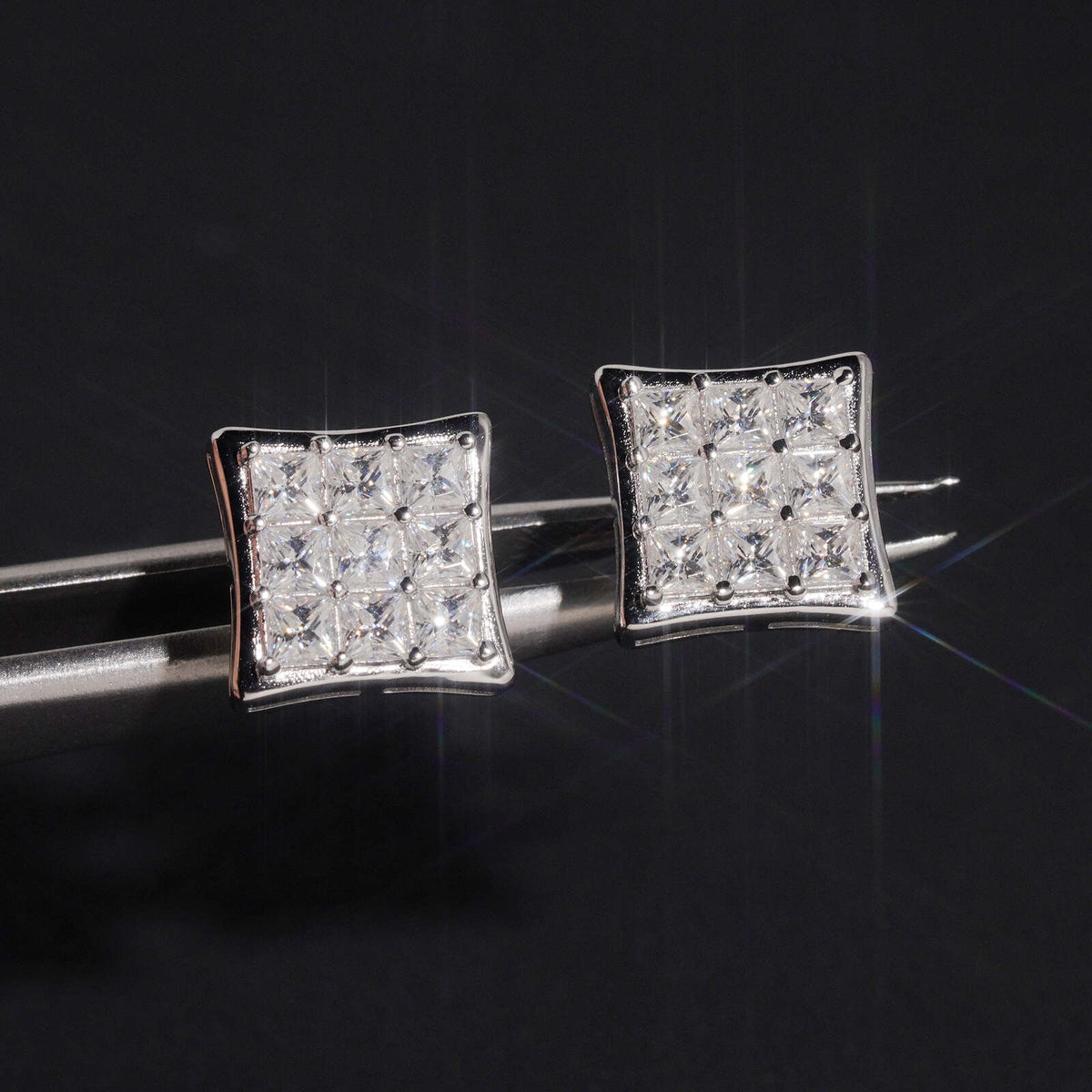 Silver iced out princess cut square cluster moissanite stud earrings held by tweezers
