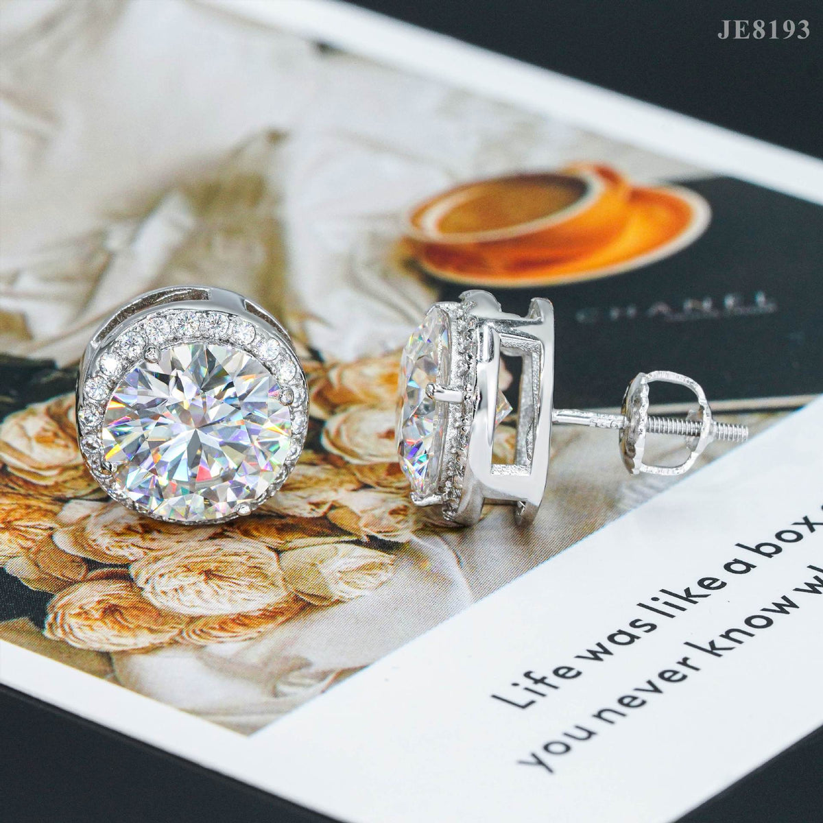 Silver iced out round solitaire halo moissanite stud earrings displayed on magazine background