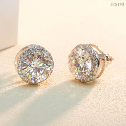 Pair of silver iced out round solitaire halo moissanite stud earrings on warm sand textured background