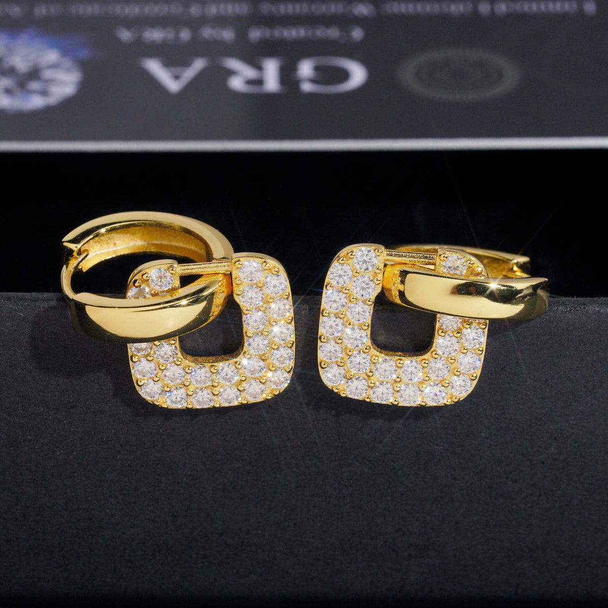 Yellow gold iced out square cushion hollow drop huggie hoop moissanite earrings with pave setting on dark background