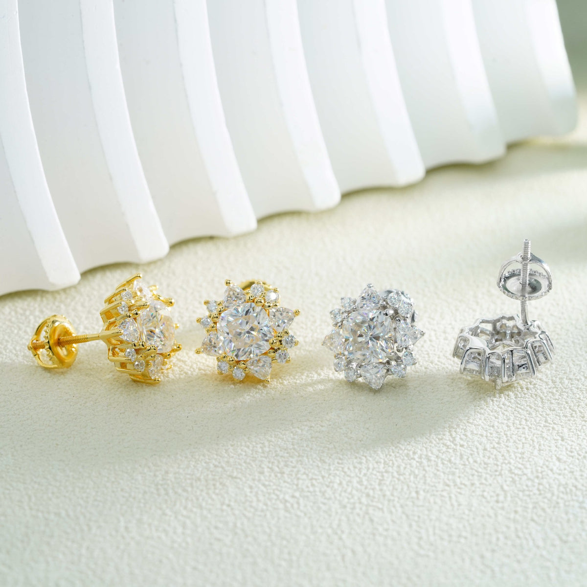 Gold and silver iced out sunburst starburst solitaire moissanite stud earrings aligned in front of white fluted backdrop