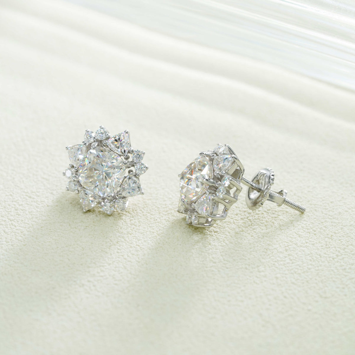 Pair of silver iced out sunburst starburst solitaire moissanite stud earrings on white textured surface
