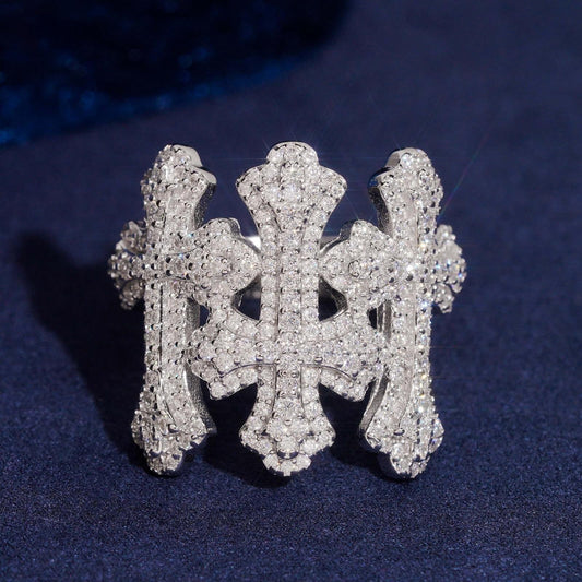 Iced out triple gothic cross moissanite ring in sterling silver resting on dark blue surface