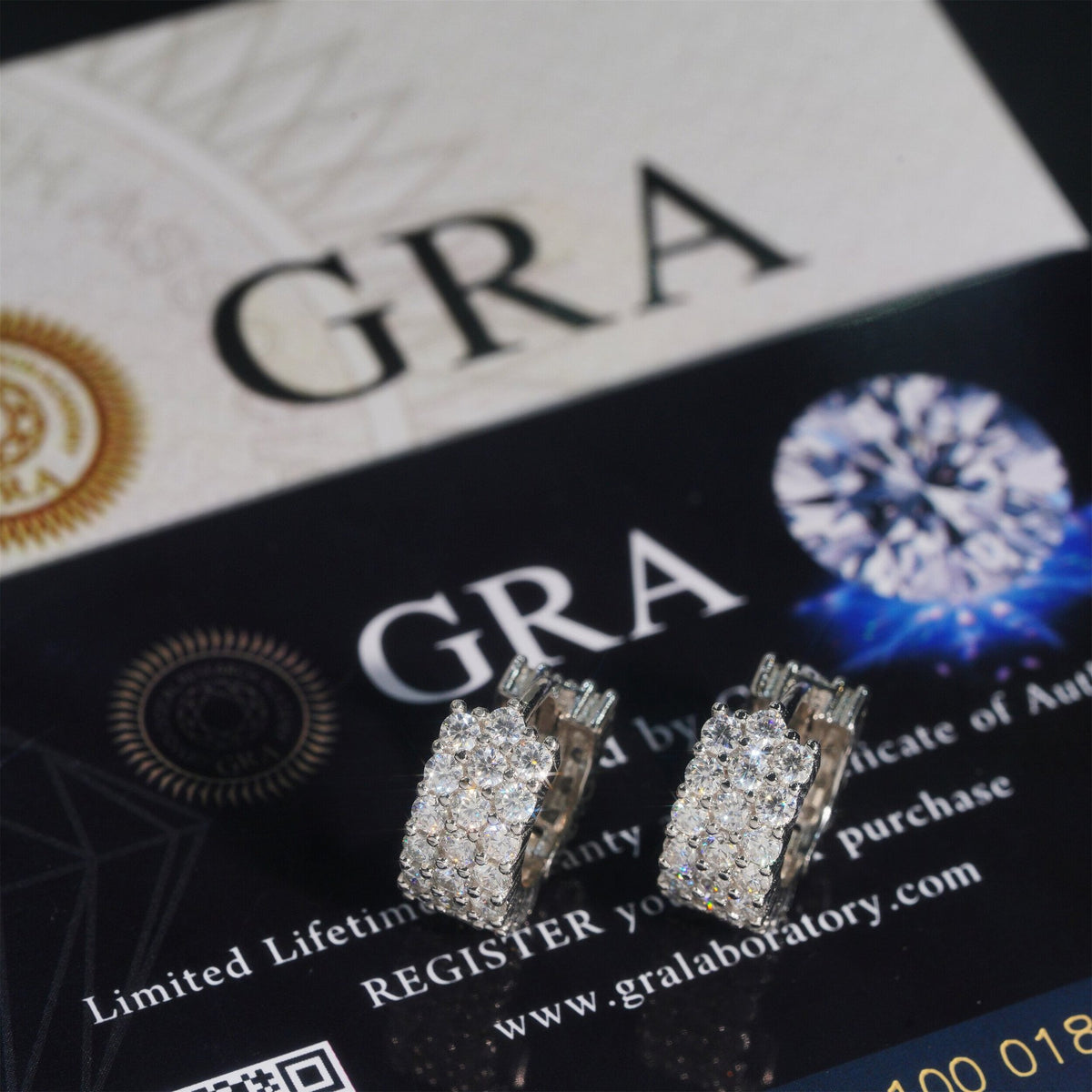 Silver iced out triple row moissanite huggie hoop earrings displayed on official GRA report card