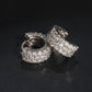 Pair of silver iced out triple row moissanite huggie hoop earrings showing hinged clasp mechanism