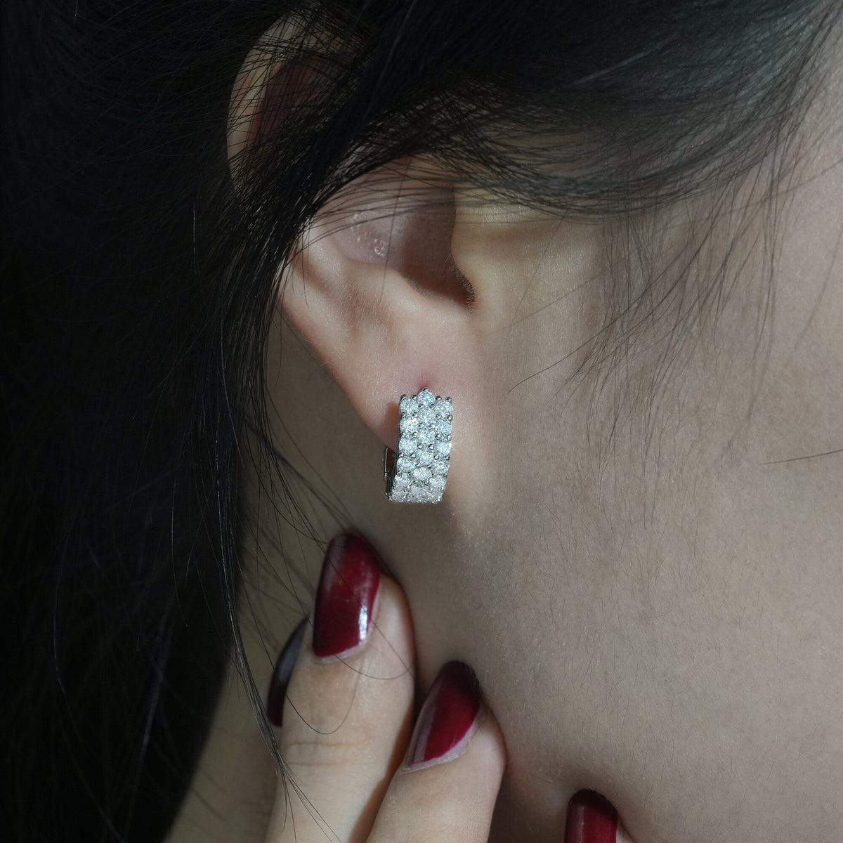 Close-up of model wearing silver iced out triple row moissanite huggie hoop earring on ear