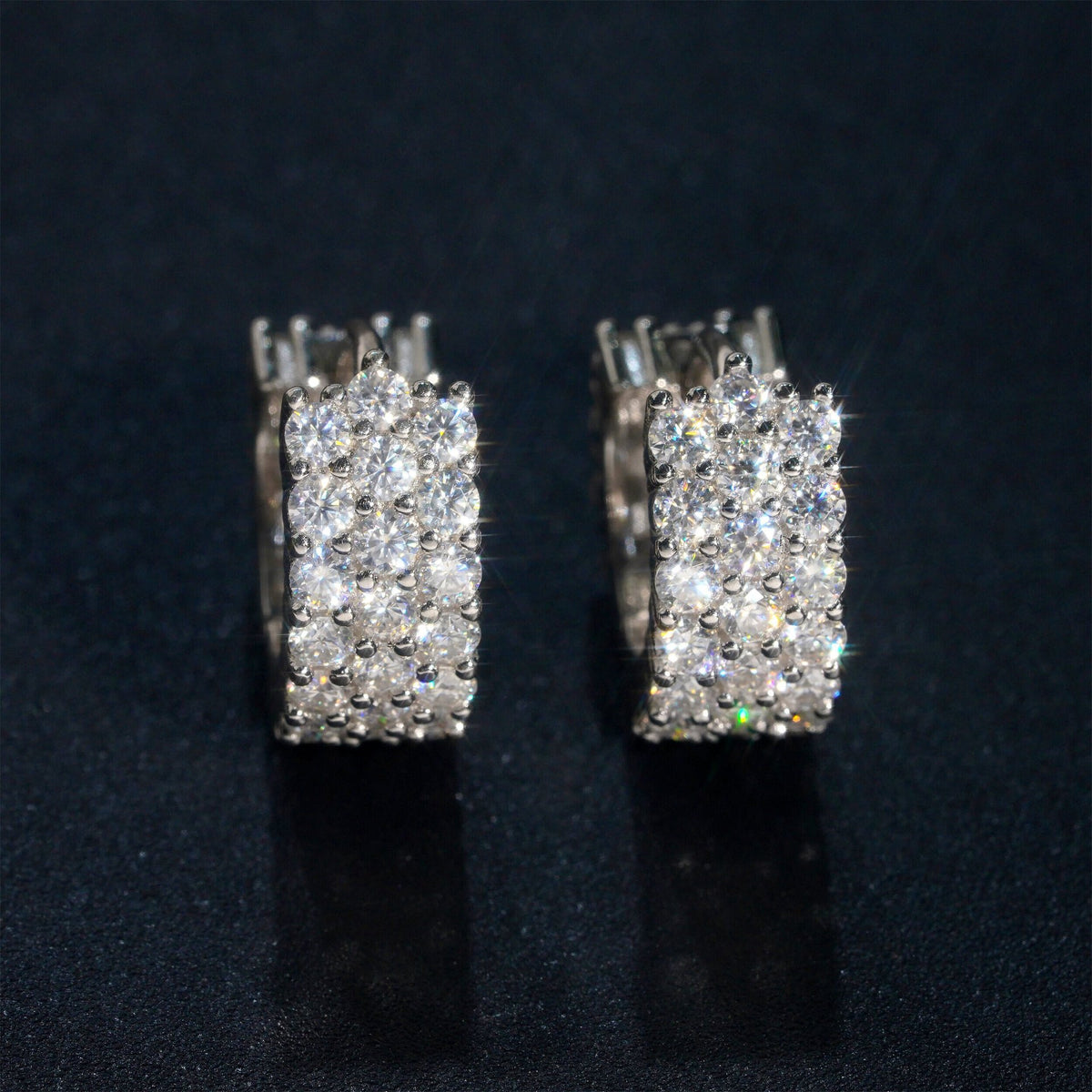 Silver iced out triple row moissanite huggie hoop earrings with pave setting on dark surface