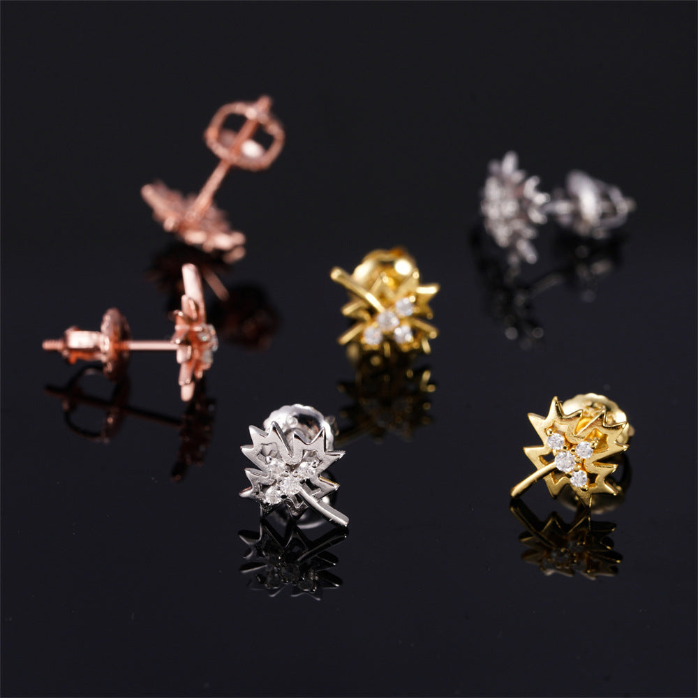 Three-tone iced out weed leaf maple leaf moissanite stud earrings showing screw back posts on black reflective surface 