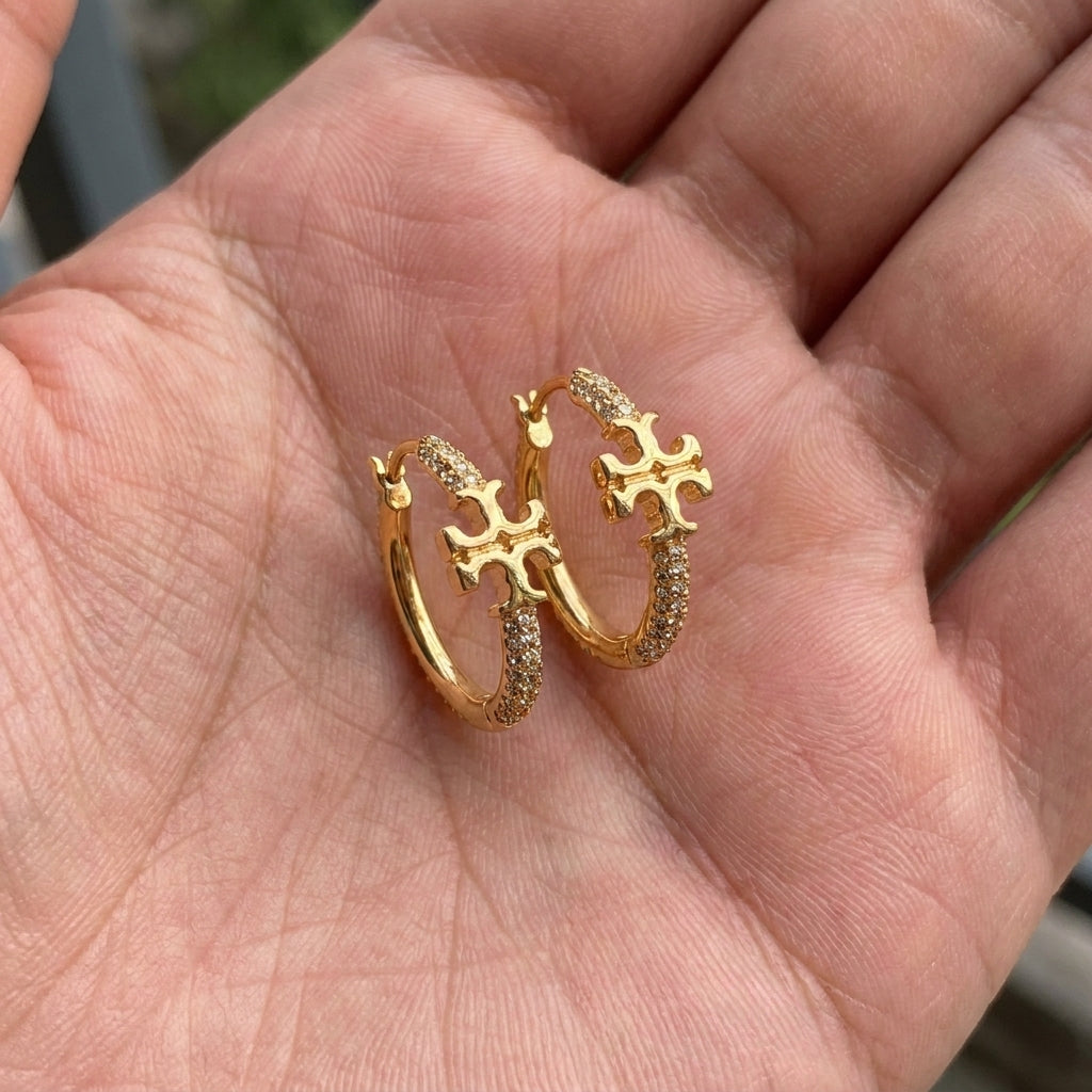 ZERRA Tory Burch Small Eleanor gold logo hoop earrings with monogram design, featuring a classic hoop style and polished finish.
