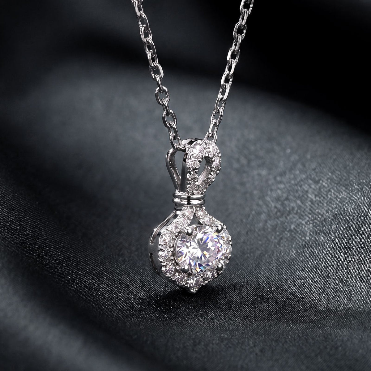 Round diamond infinity knot halo pendant necklace displayed on dark background.
