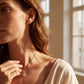 Model wearing round diamond infinity knot halo pendant necklace near window.