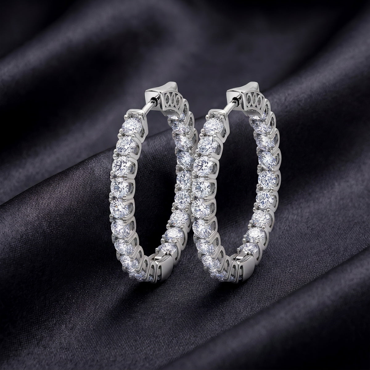 Pair of inside-out round cut lab grown diamond hoop earrings resting on dark black silk