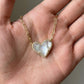 The Kendra Scott Ari asymmetric white mother of pearl heart necklace held in a palm for size and quality reference.