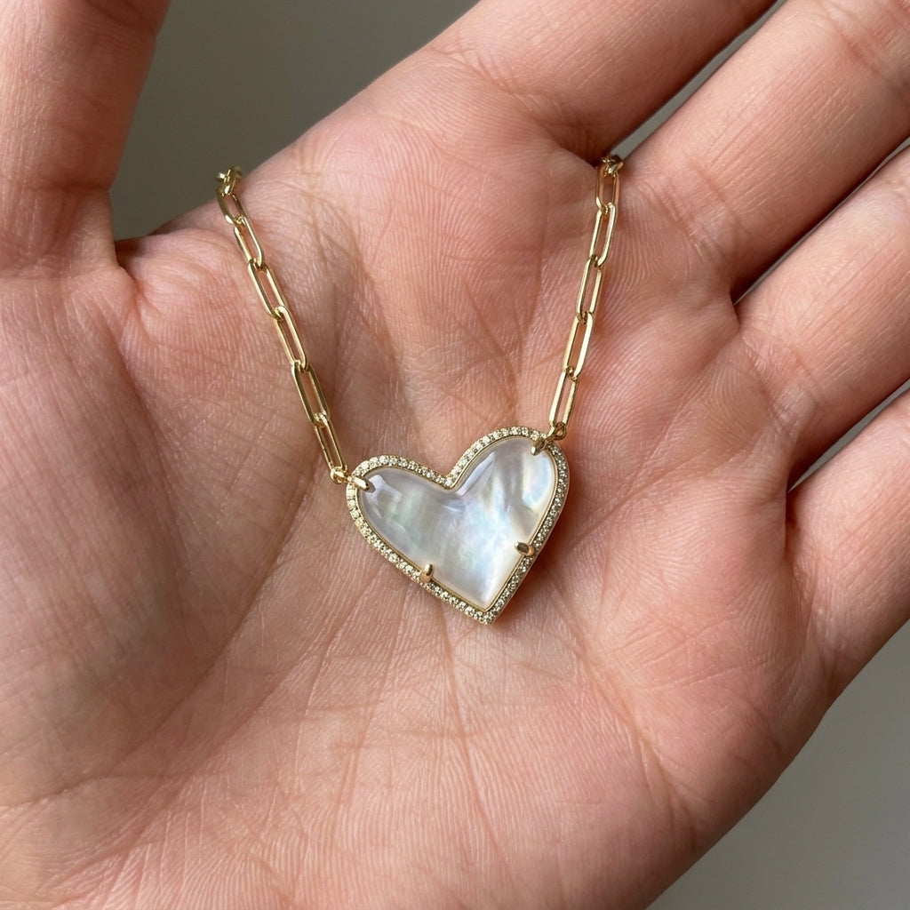 The Kendra Scott Ari asymmetric white mother of pearl heart necklace held in a palm for size and quality reference.
