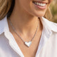 Front view of a model wearing the silver Kendra Scott Ari heart pendant necklace with a professional white button-down shirt.