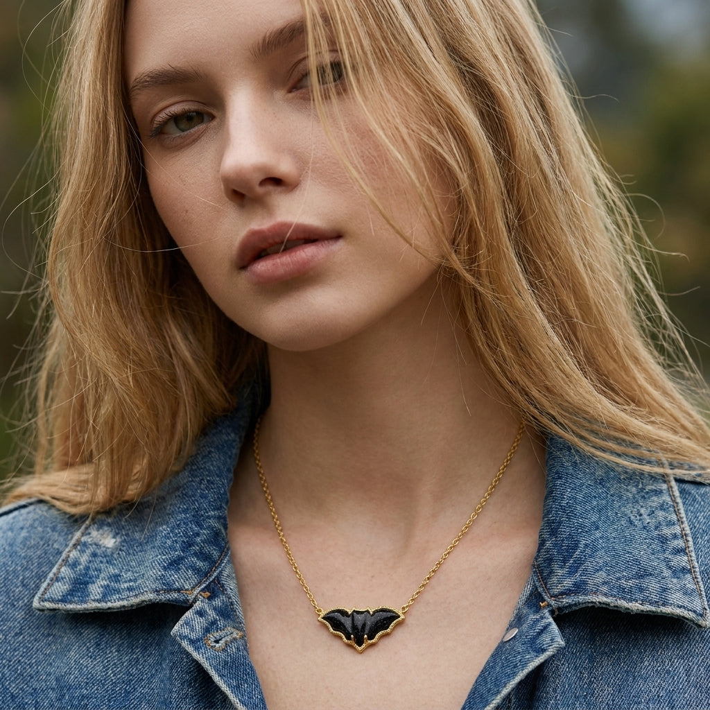 A model wearing the Kendra Scott Bat gold pendant necklace styled with a denim shirt in outdoor natural light.