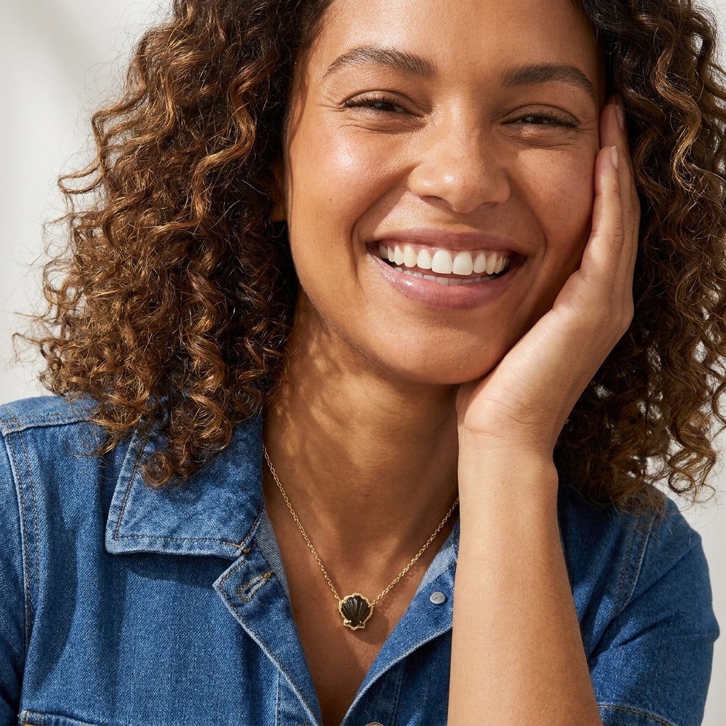 Smiling model showcasing the gold and black mother of pearl Brynne shell pendant necklace.