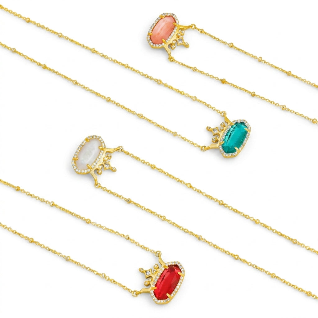 A collection of four Kendra Scott x Disney Elisa Princess crown necklaces in red, green, pink, and white options.