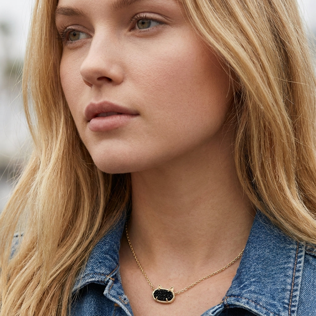 A close-up of a model wearing the Kendra Scott Elisa cat gold necklace in black drusy, styled with a denim jacket.