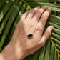 The Kendra Scott Elisa cat gold and black necklace held on a hand against a tropical palm leaf background for scale.