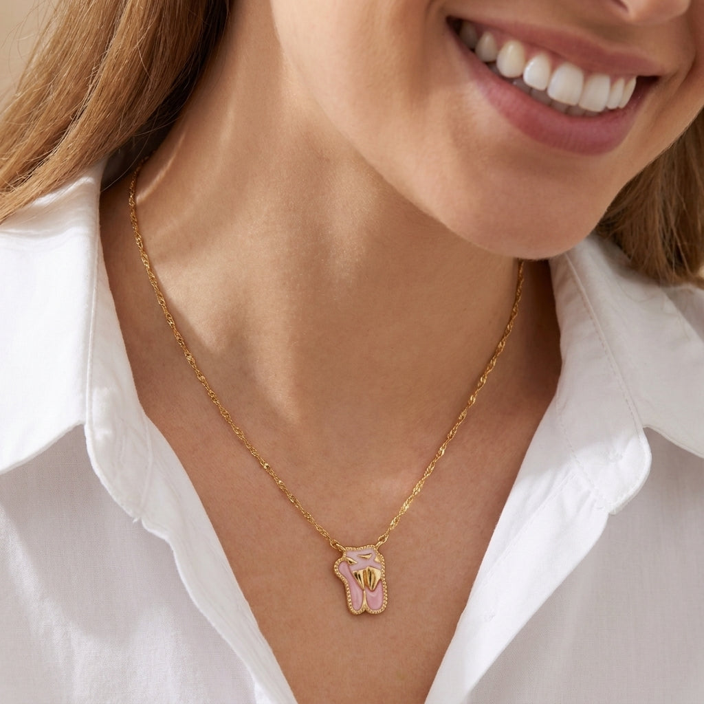 Smiling model wearing the gold Kendra Scott ballet slippers pendant necklace with a white blouse.